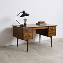 Vintage teak wood desk with a lamp and books against a white wall