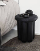 The Phant Side table made of Black Mango Wood side table placed next to a bed.