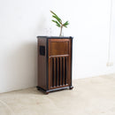 A converted Art Deco radio cabinet with a single front door and vertical slatted detailing, standing on a light concrete floor against a white wall with a small plant on top.