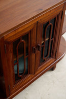 A close-up of a dark reddish-brown wooden cabinet with two doors featuring decorative geometric cutouts in the glass panels, set against a light-colored floor.