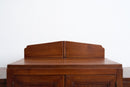 A close-up of a dark brown wooden cabinet or dresser showing the top surface and a decorative backrest panel against a plain white wall.