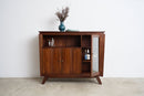 An Art Deco sideboard with a warm brown finish, featuring open shelves, a glass-front door, and tapered legs, styled with a blue vase on top against a white wall.