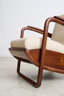 An Art Deco Streamline Moderne armchair with a warm brown teak frame and cream-colored seat and back cushions, shown in a close-up studio shot.