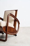 An Art Deco Streamline Moderne wooden armchair with curved dark teak frames and cream-colored leather cushions, shown in a minimalist studio setting.
