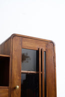 Close-up of an Art Deco wooden cabinet with a warm brown walnut finish, featuring a glass door with vertical metal handles and a brass knob.