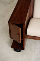 Close-up of a dark brown wooden side cabinet attached to an Art Deco with cream-colored cushions, showing the open door and shelf detail.