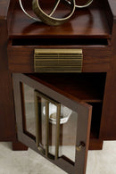 A close-up of a converted Art Deco speaker cabinet with a glass-front lower door, brass hardware, and an open drawer above, set against a light stone floor.
