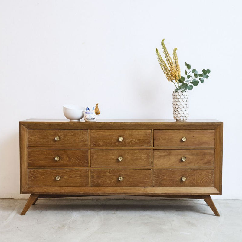 Midcentury teak wood vintage dresser with decorative items against a white wall