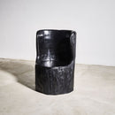 Black sculptural tree trunk chair on a textured surface with a plain background