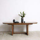 Vintage extending wooden dining table with a plant and decorative items against a white wall.