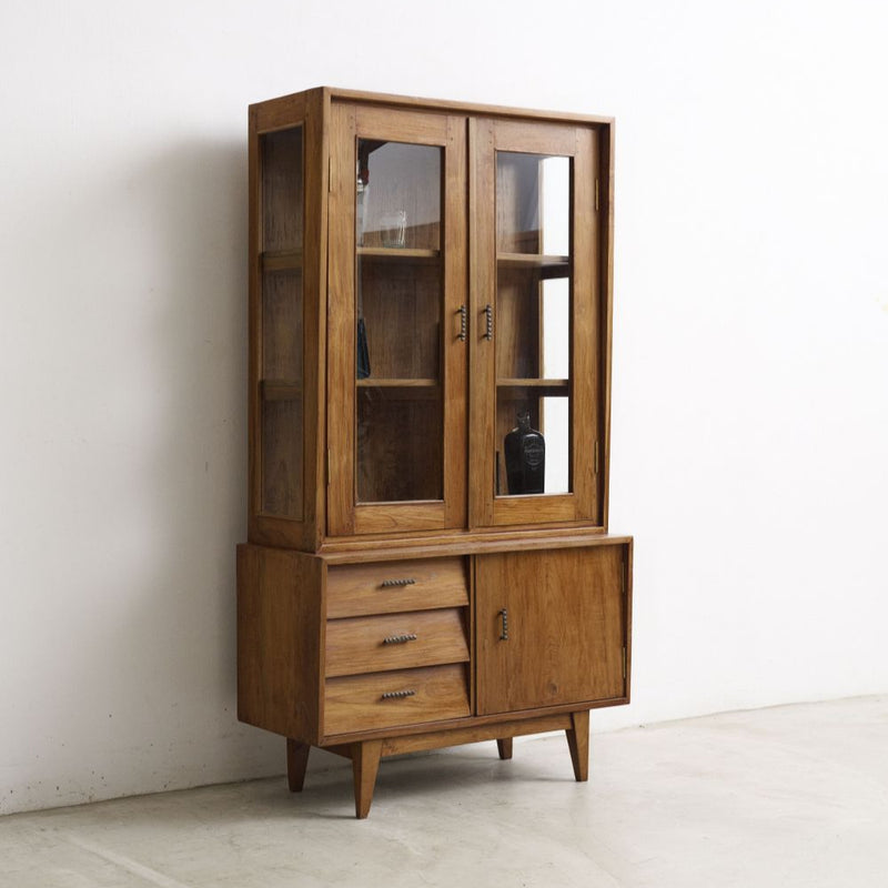 Vintage wooden cabinet with glass doors and drawers against a white wall.
