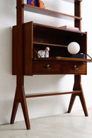 Mid-century modern wooden writing desk with open shelving, two drawers, and angled legs, styled with books, a mug, and a white globe lamp against a white wall.
