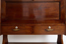 A close-up of a dark brown wooden writing desk with two drawers and brass handles, set against a plain white background.