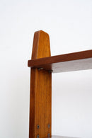 Close-up detail of a mid-century modern wooden shelf corner, showing a warm brown teak wood grain finish, a tapered top, and metal shelf brackets against a plain white background.