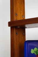 Close-up of a wooden shelving unit with a medium brown wood grain finish, showing the shelf bracket hardware and a blue decorative item partially visible at the bottom right.