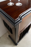 Close-up of a dark wood and black cabinet corner with decorative molding, showing part of a stool base and two wine glass bases on top.