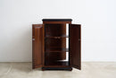 A dark brown wooden cabinet with two open doors and three interior shelves, photographed against a plain white wall and light concrete floor.