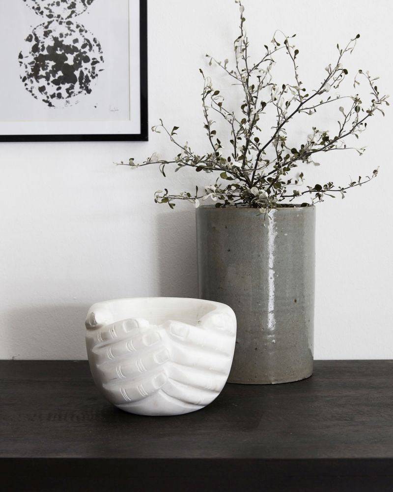 The hands bowl is place next to a vase of flowers on a side board as decor.